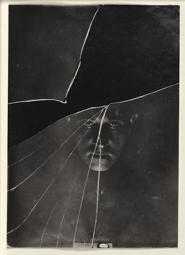 Witkiewicz’s shadowy face on a dark background stares at the viewer through cracks