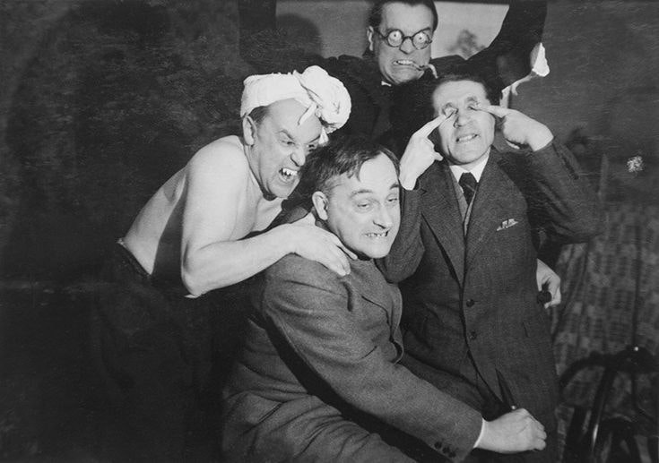 The four men in the photograph climb on one another making faces
