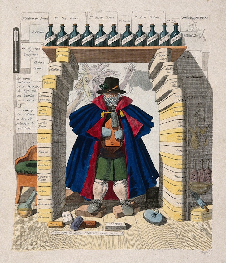 A man wears a mask while huddling under an arch made from boxes and bottles of medicinal materials