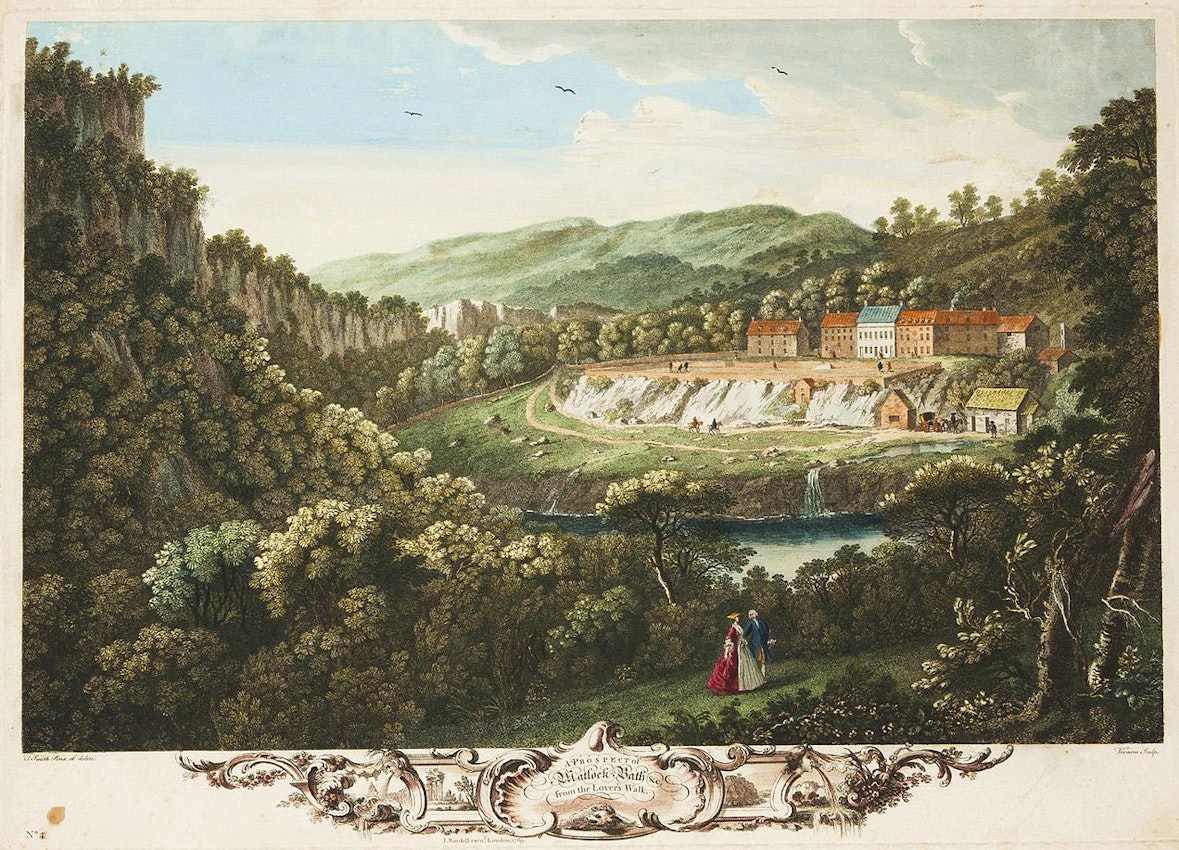 Two human figures in the foreground with the buildings of the bath in the background