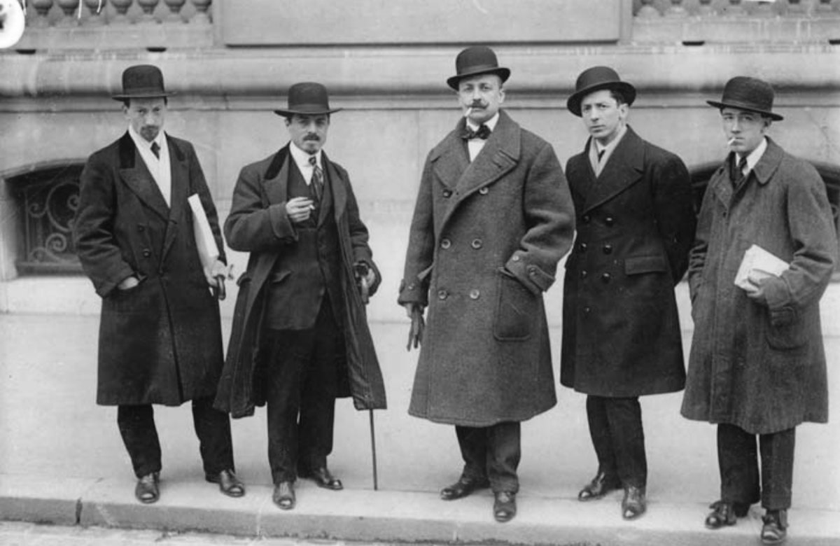 Five men posing on the sidewalk in hats and coats