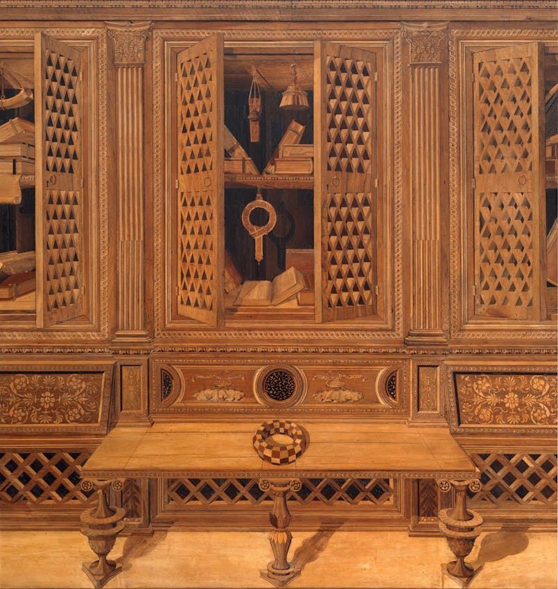 Wooden cabinet with latticed doors displaying books and ornate carvings, featuring decorative columns and a checkered ring on the tabletop below.