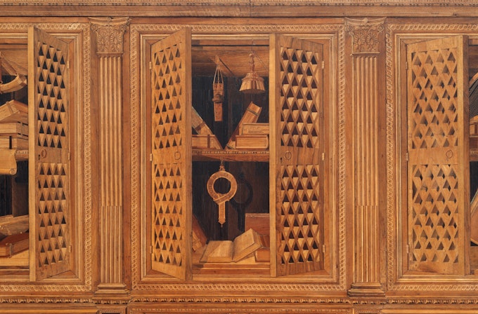 Intarsia depicting wooden cabinet with latticed doors revealing open books and hanging instruments inside, surrounded by ornately carved columns and decorative trim.