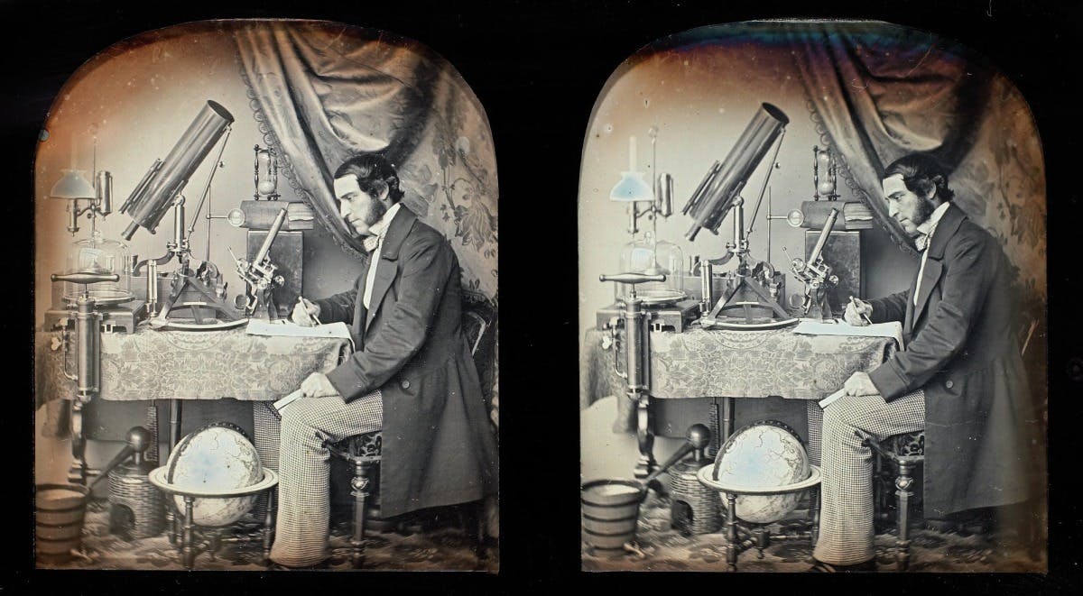 A stereoscopic pair of photographs showing a man in formal attire writing at a desk with scientific instruments including a telescope and globe nearby.