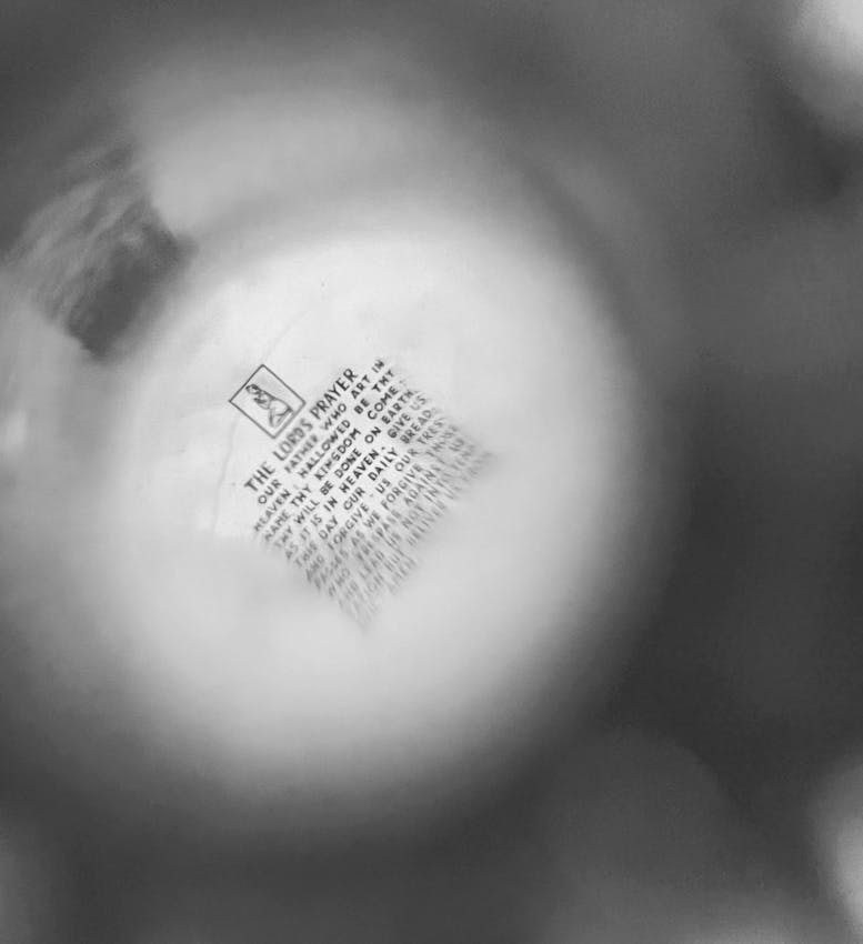 Close-up view of text showing portions of The Lord's Prayer through a circular magnifying lens with blurred background.
