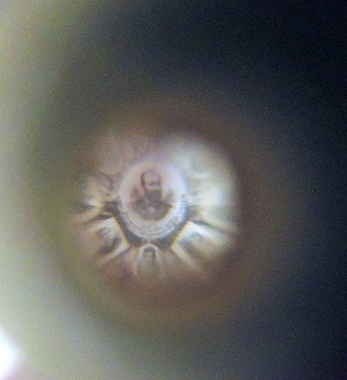 Circular view through optical device showing a portrait of a bearded man surrounded by a radiant effect against a dark background.