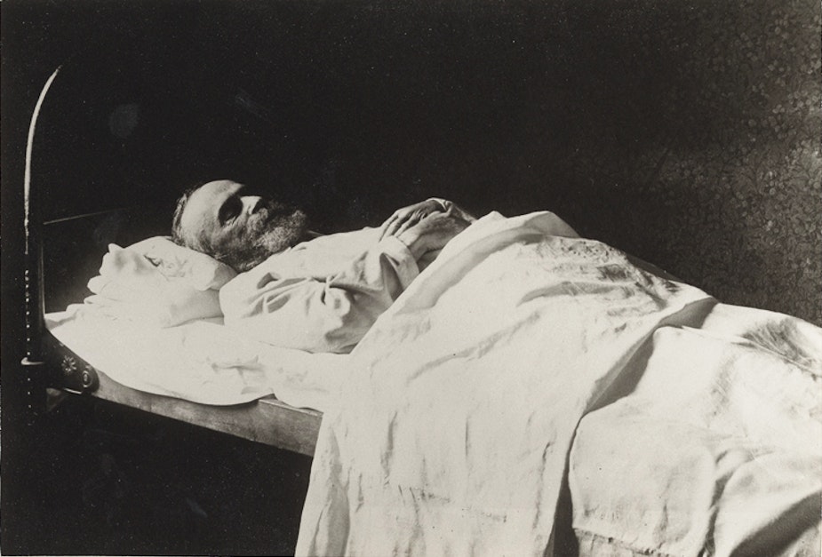 James lying in bed with blanket draped over his body