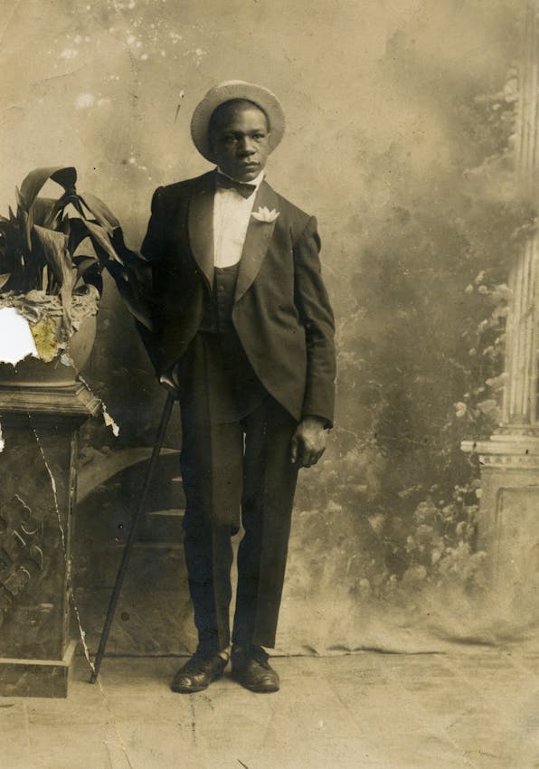 Torn studio photograph of Raúl Grigera in a dinner jacket, holding a cane