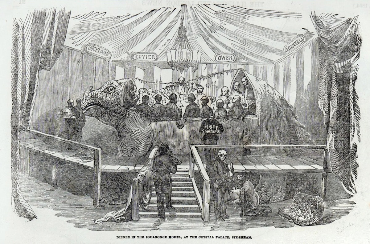 Illustration of a banquet held inside an iguanodon model surrounded by banners with names such as ‘OWEN’ and ‘CUVIER.’