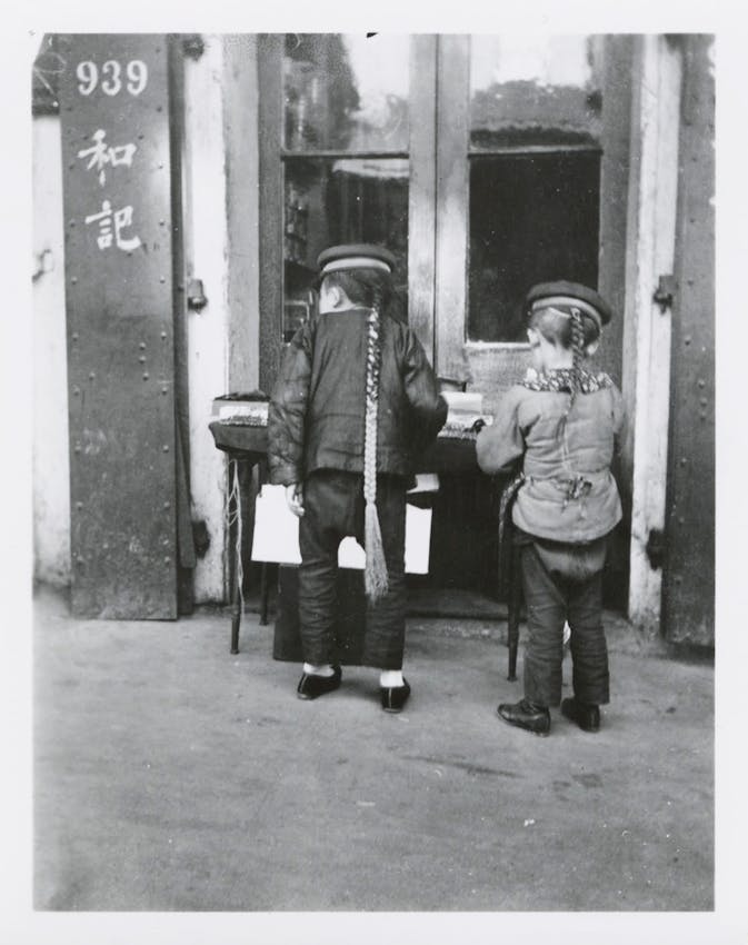 Two boys with long braided queues standing in front of a storefront numbered 939 with Chinese characters