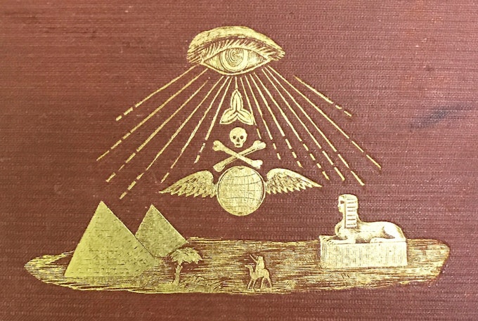 Embossed golden illustration on a maroon book cover featuring an eye emitting rays towards a skull and crossbones over wings, with pyramids, a palm tree, a sphinx, and a person in the foreground.