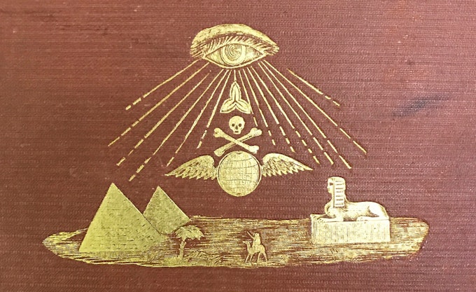 Embossed golden illustration on a maroon book cover featuring an eye emitting rays towards a skull and crossbones over wings, with pyramids, a palm tree, a sphinx, and a person in the foreground.