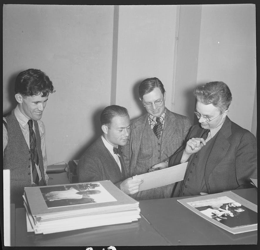 Men gathered round looking at photographs