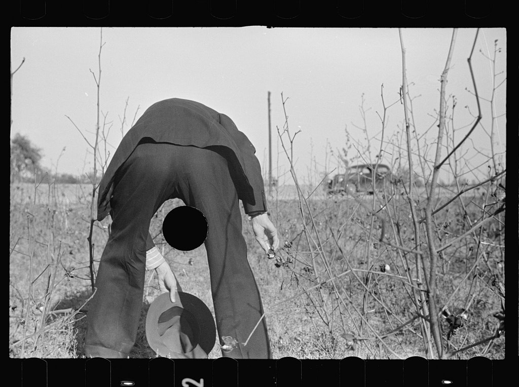 man viewed from behind bending over in a field, the punctured hole between his legs