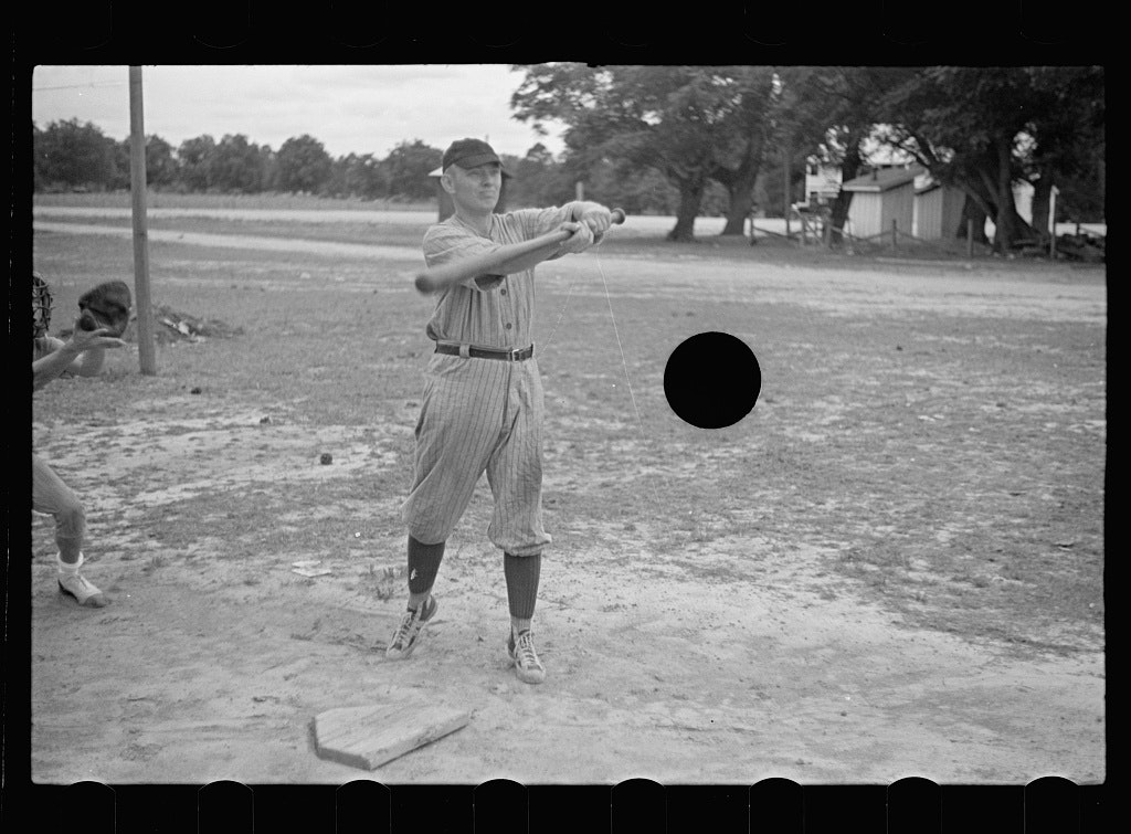black and white photo of a man swinging a baseball bat, the punctured hole where the ball might be
