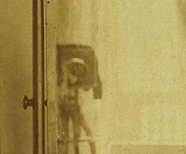 Close-up of a reflection in a mirror, showing a blurred image of old photographic equipment, captured in a sepia-toned photograph
