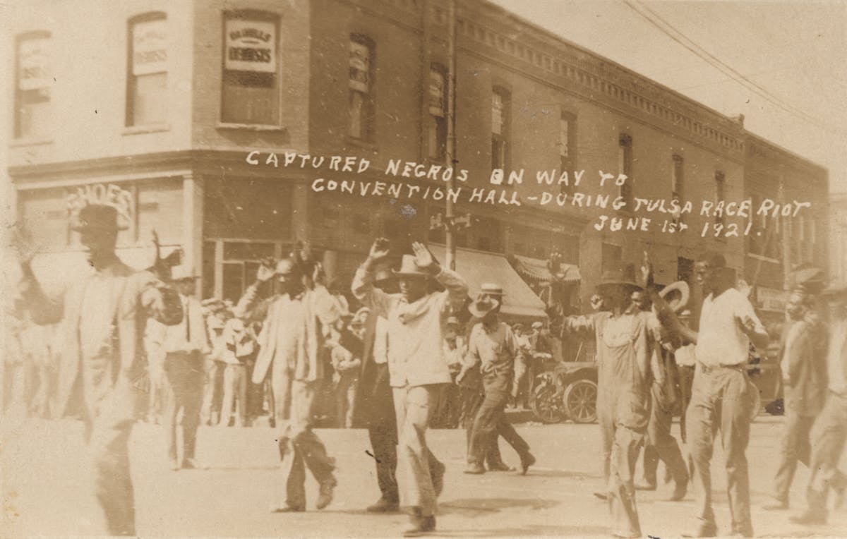 Black men being marched with their hands raised over heads down city street