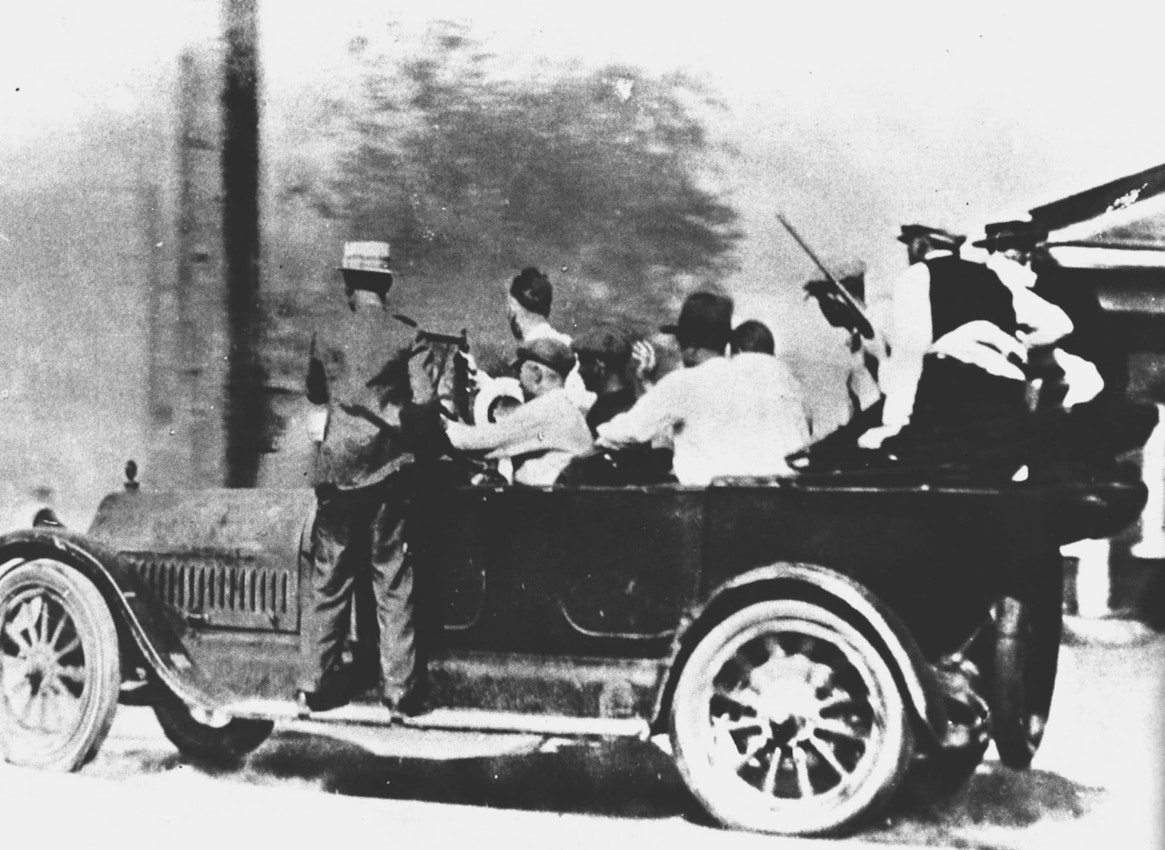 Automobile loaded with men, some holding guns