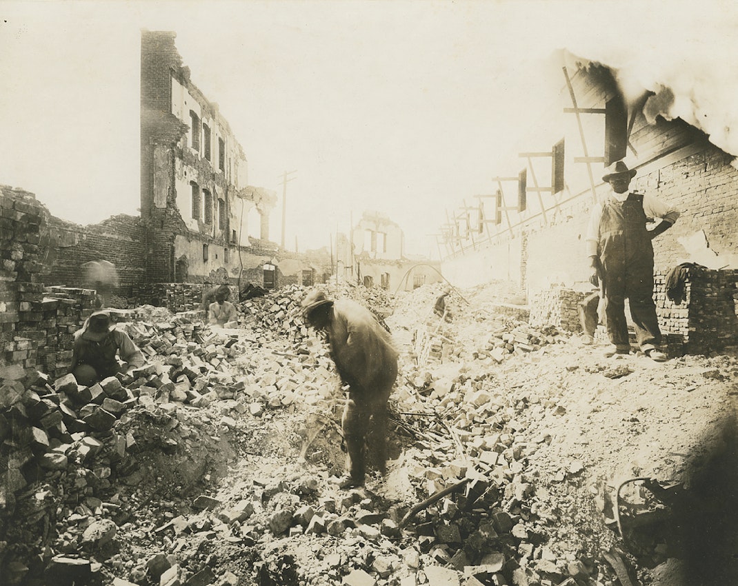 Photograph of four men digging in fallen and burned building